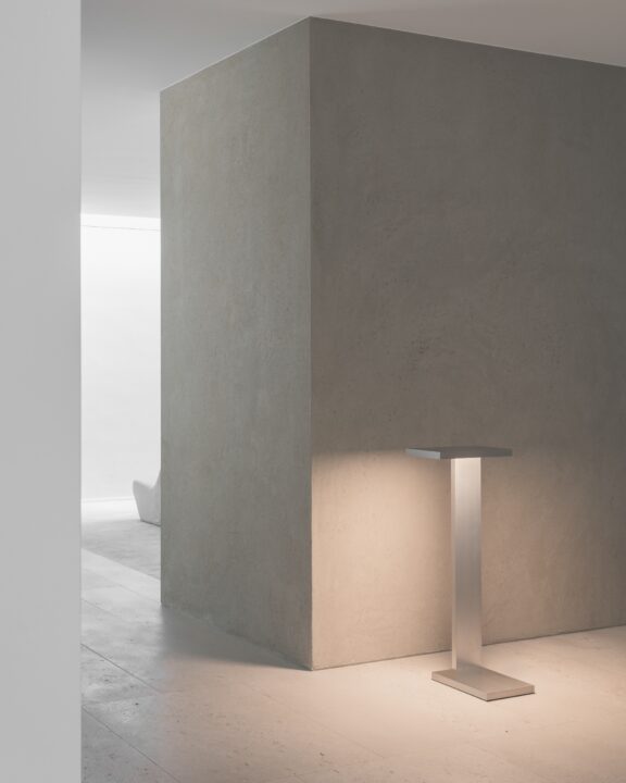 Die Stehleuchte Furtiv LH Ozone beleuchtet einen Raum mit grauen, gewachsten Betonwänden.