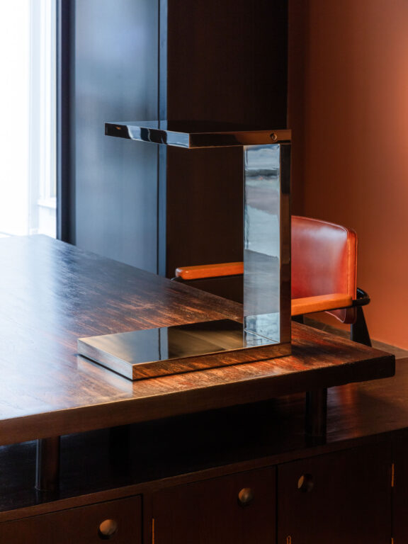Furtiv LP Ozone Tischlampe aus verspiegeltem Nickel auf einem Holzschreibtisch in einem orangefarbenen Raum