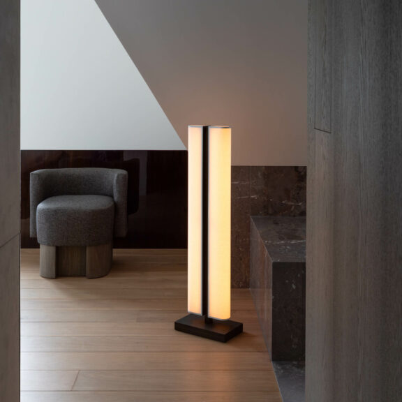 The Tennessee LH floor lamp illuminates a hallway in Château Lannoo, featuring black marble details and an anthracite gray armchair.