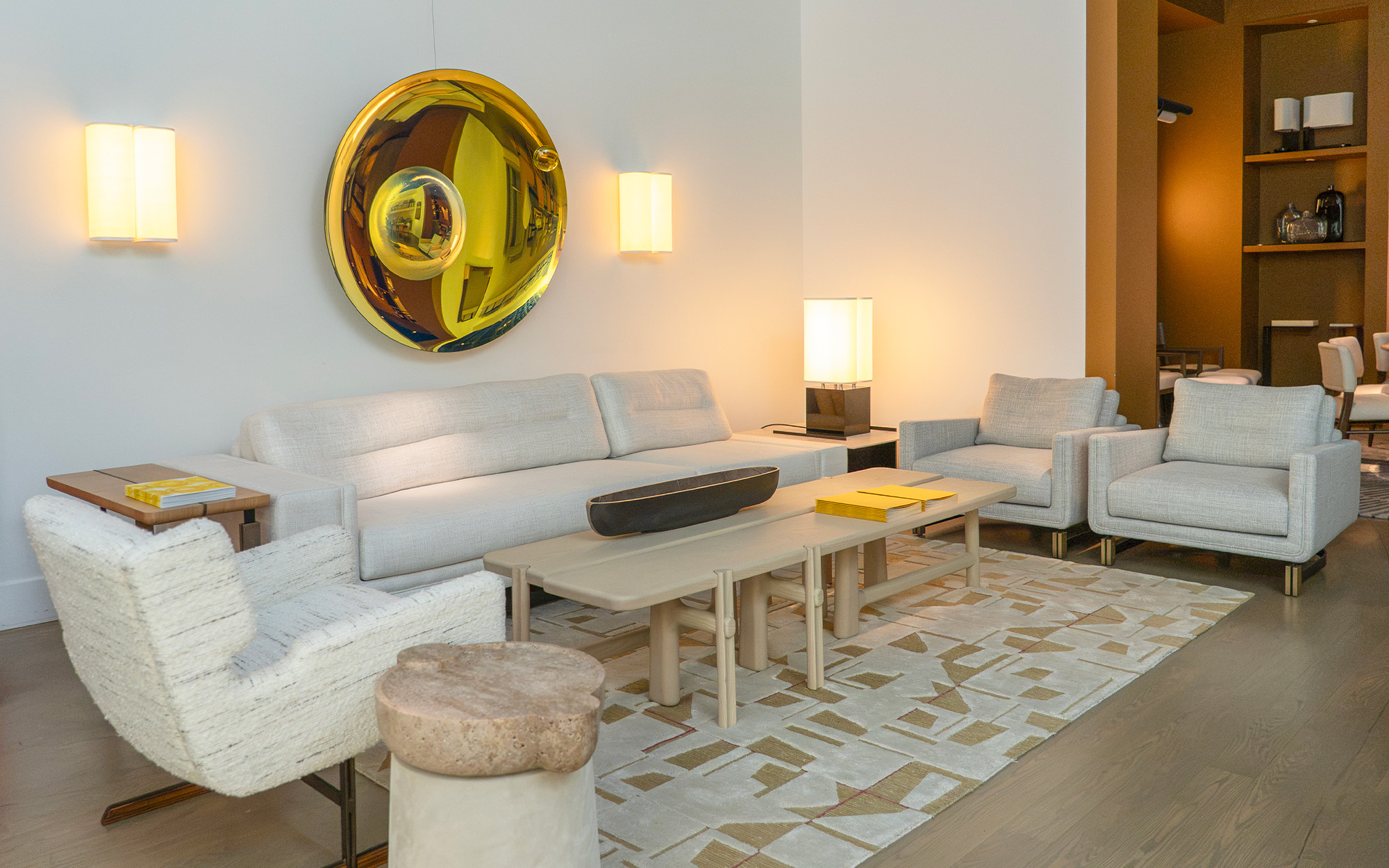 A living room decorated in shades of beige and gray is lit by two wall sconces and a table lamp from the Brasilia collection, designed by Michel Boyer for Ozone