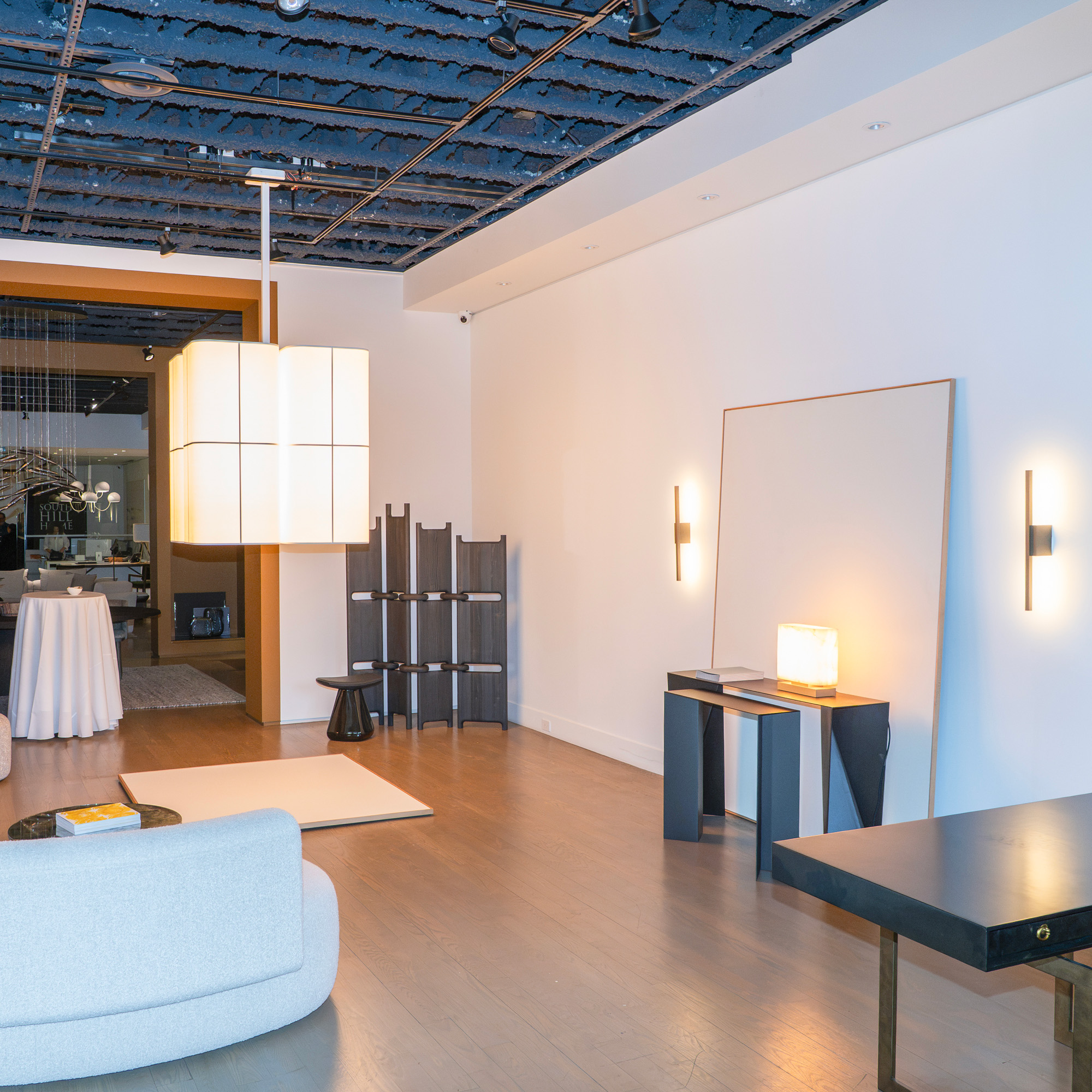 The exhibition features a Brasilia L chandelier, two Untitled A wall sconces, and an Embrun LP table lamp, all designed by Ozone.